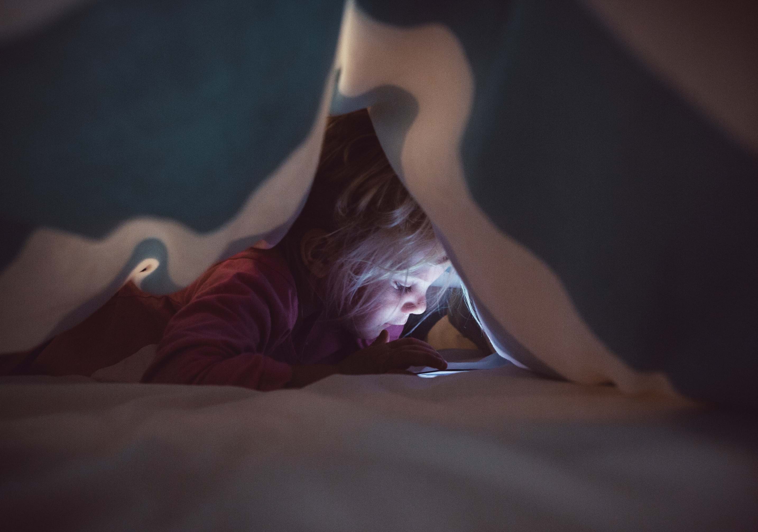 Girl reading on a phone under a blanket 