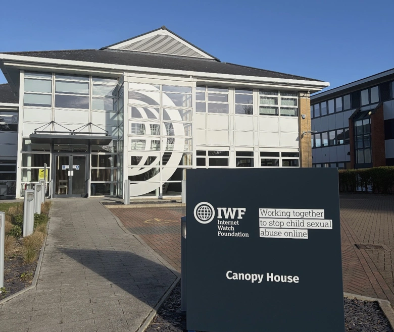 Image showing the outside of the new IWF office building on Cambridge Science Park. There is a blue sign outside with the IWF logo and building name, Canopy House. There is a big white globe decal across the front windows. 