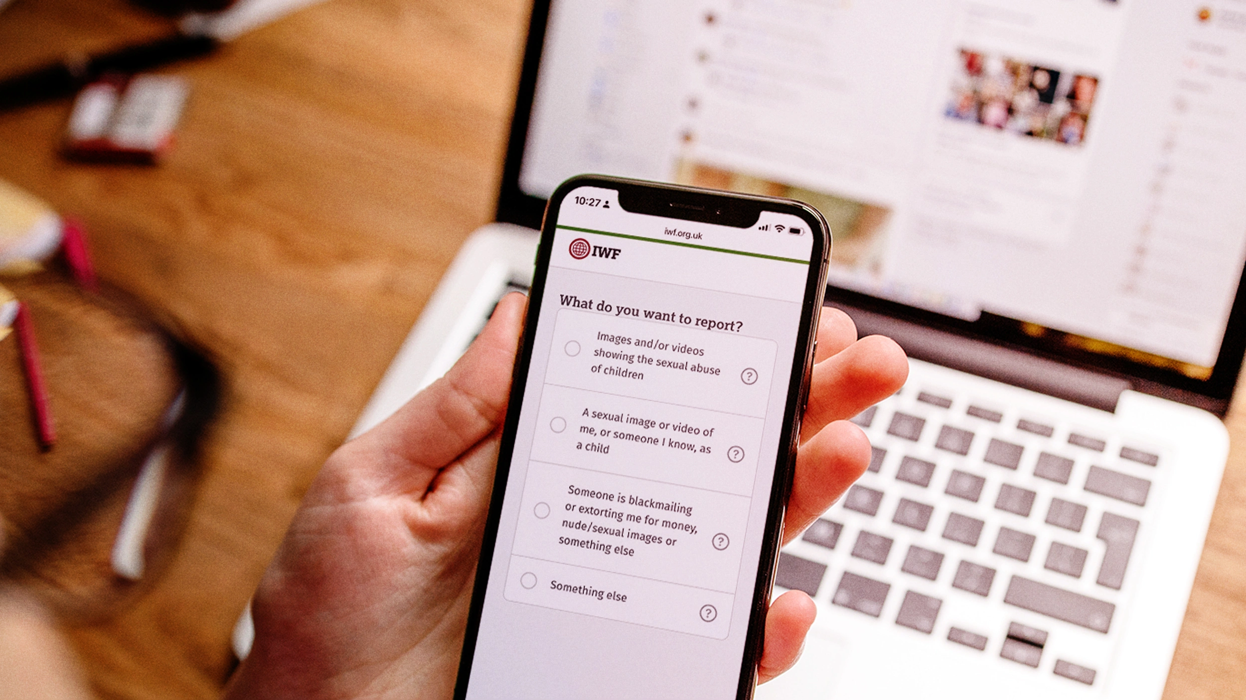IWF's UK Report Page being accessed via a mobile showing a laptop and keyboard in the background.
