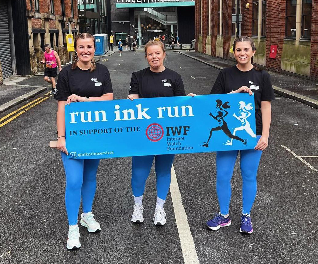 Fundraising 'Ink Print Services' heroes proudly holding an IWF branded banner.