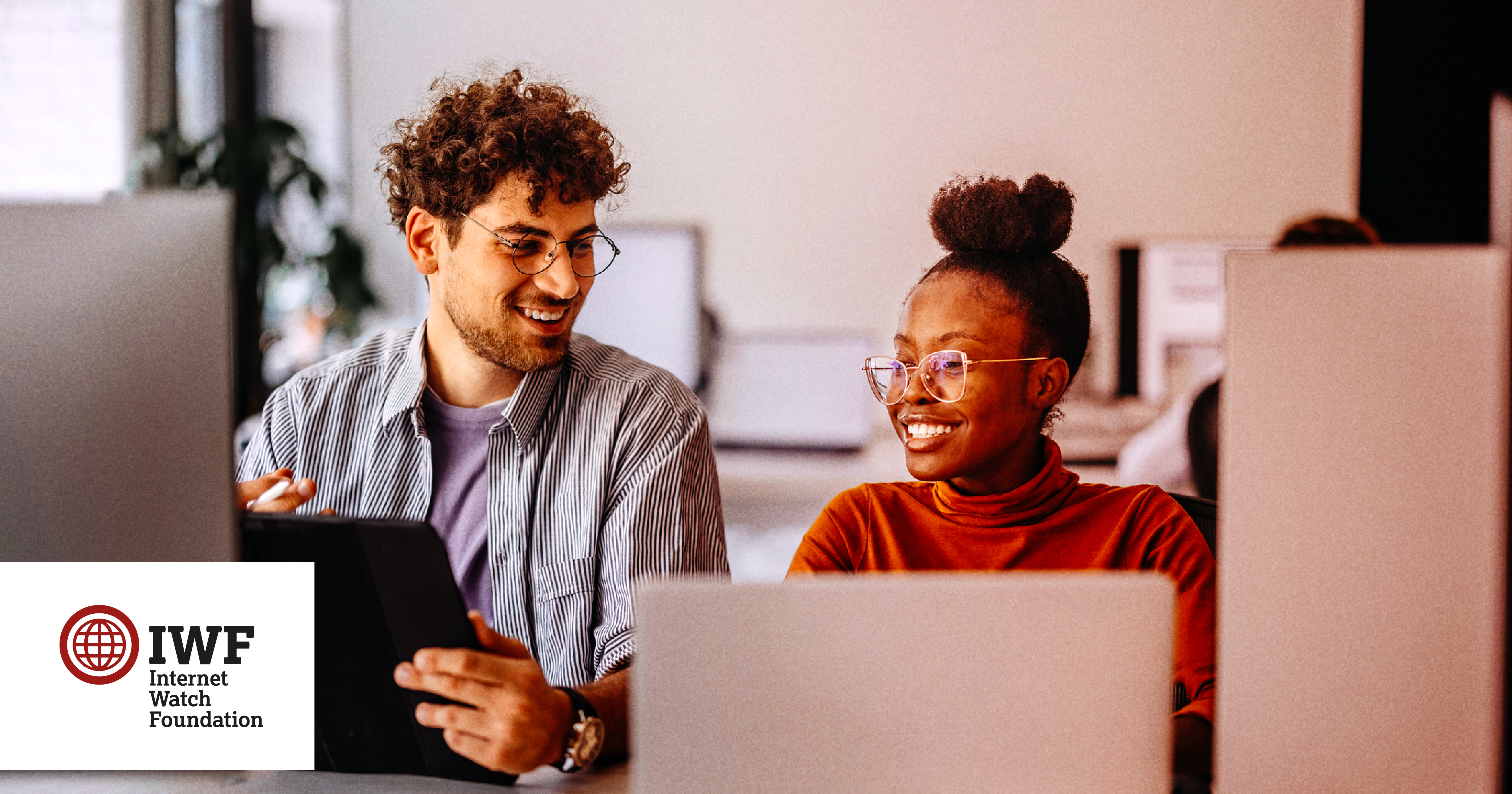 Two colleagues on computers laughing together in an office