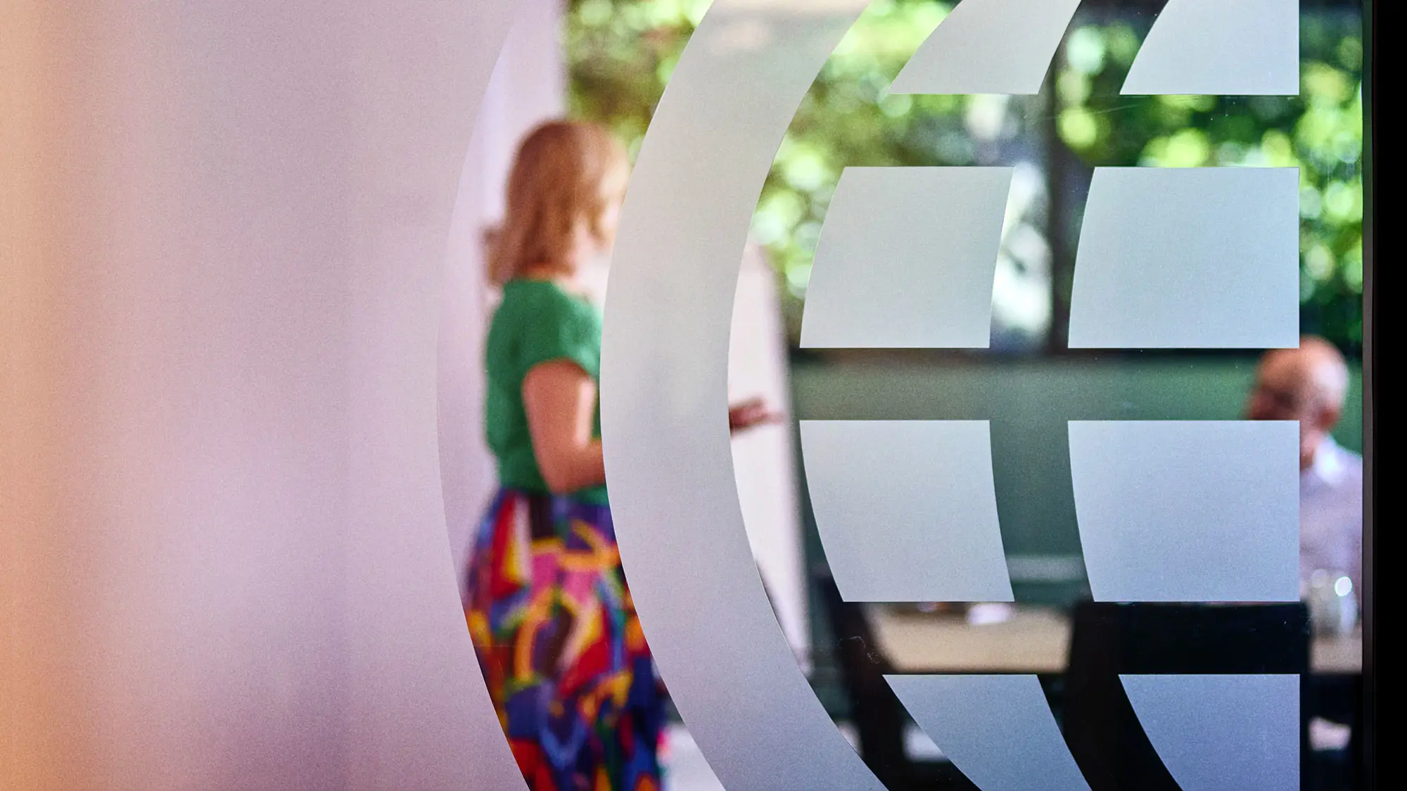 Two people talking in an IWF office behind a window with a decal of the IWF logo globe