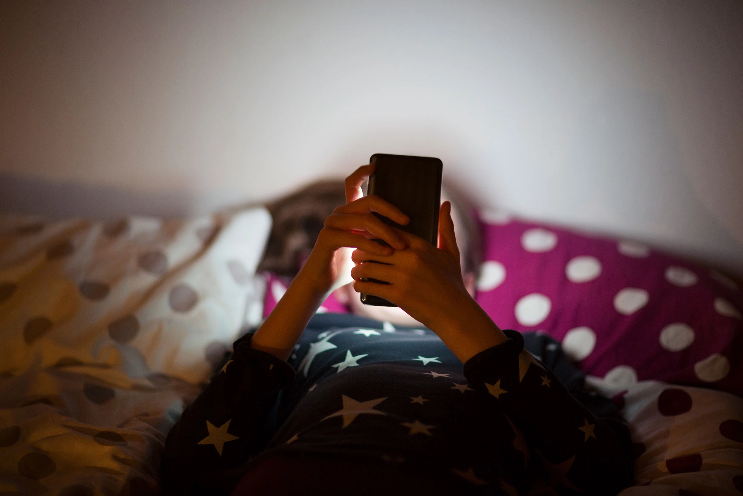 Child looking at phone on bed
