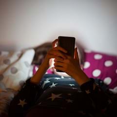 Girl looking at phone sitting on a bed