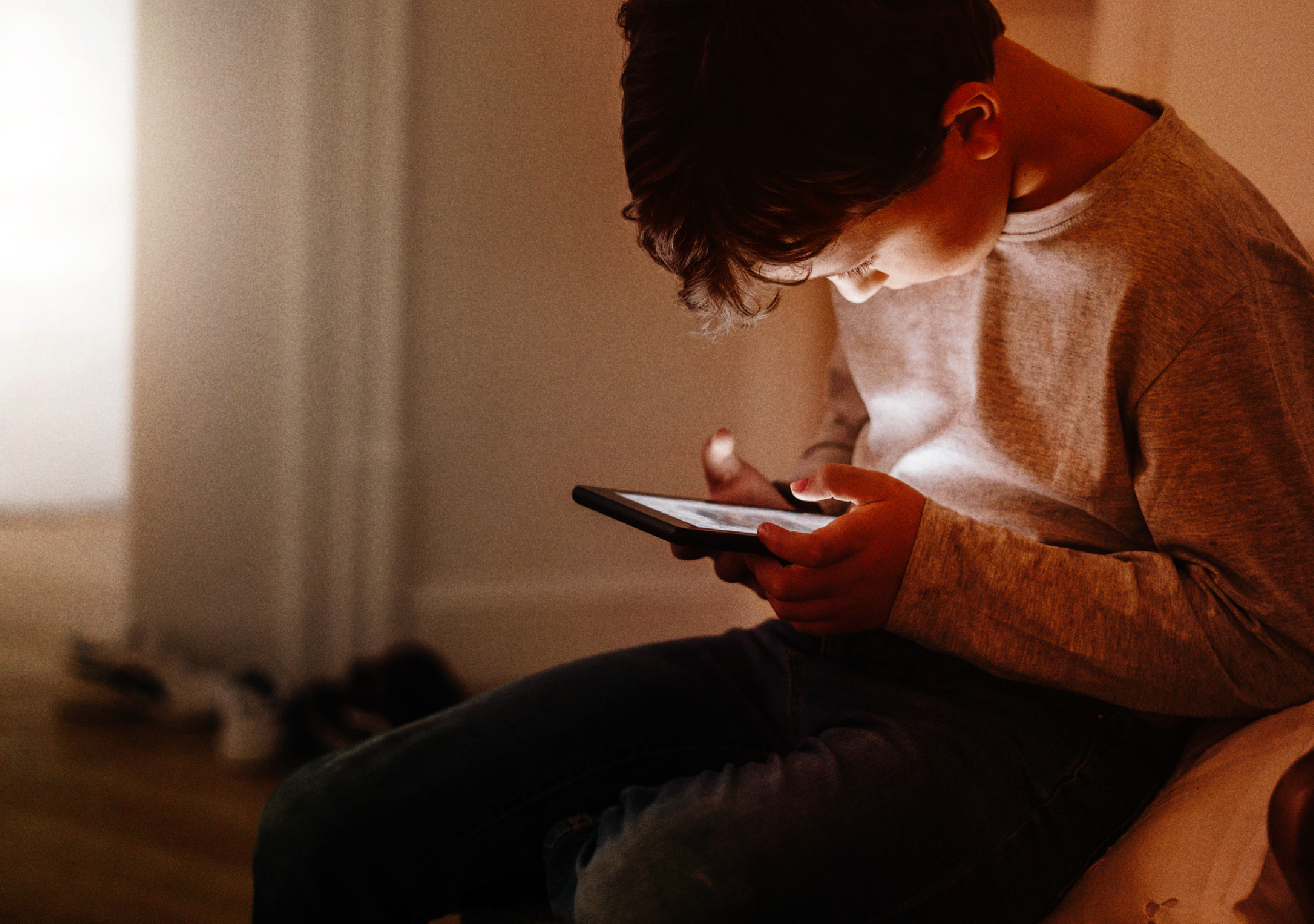 Young boy on his phone alone in shadowy room