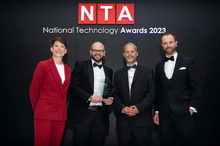 Four people wearing smart clothes standing infront of the National Technology Awards logo holding an award